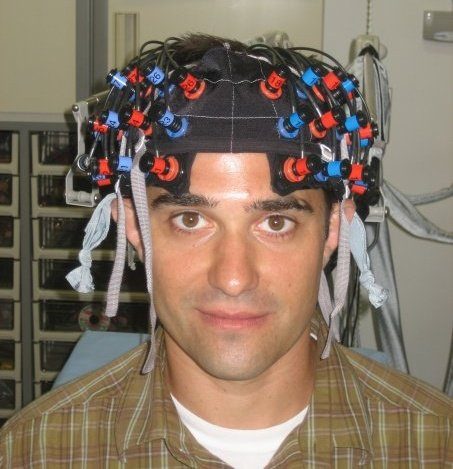 Adam wearing an fNIRS cap fitted with optodes and fiber-optic cables