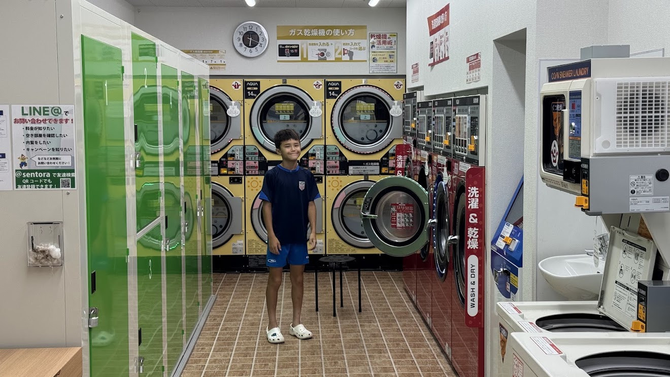 My son standing in a bright Japanese coin laundromat lined with washers and dryers
