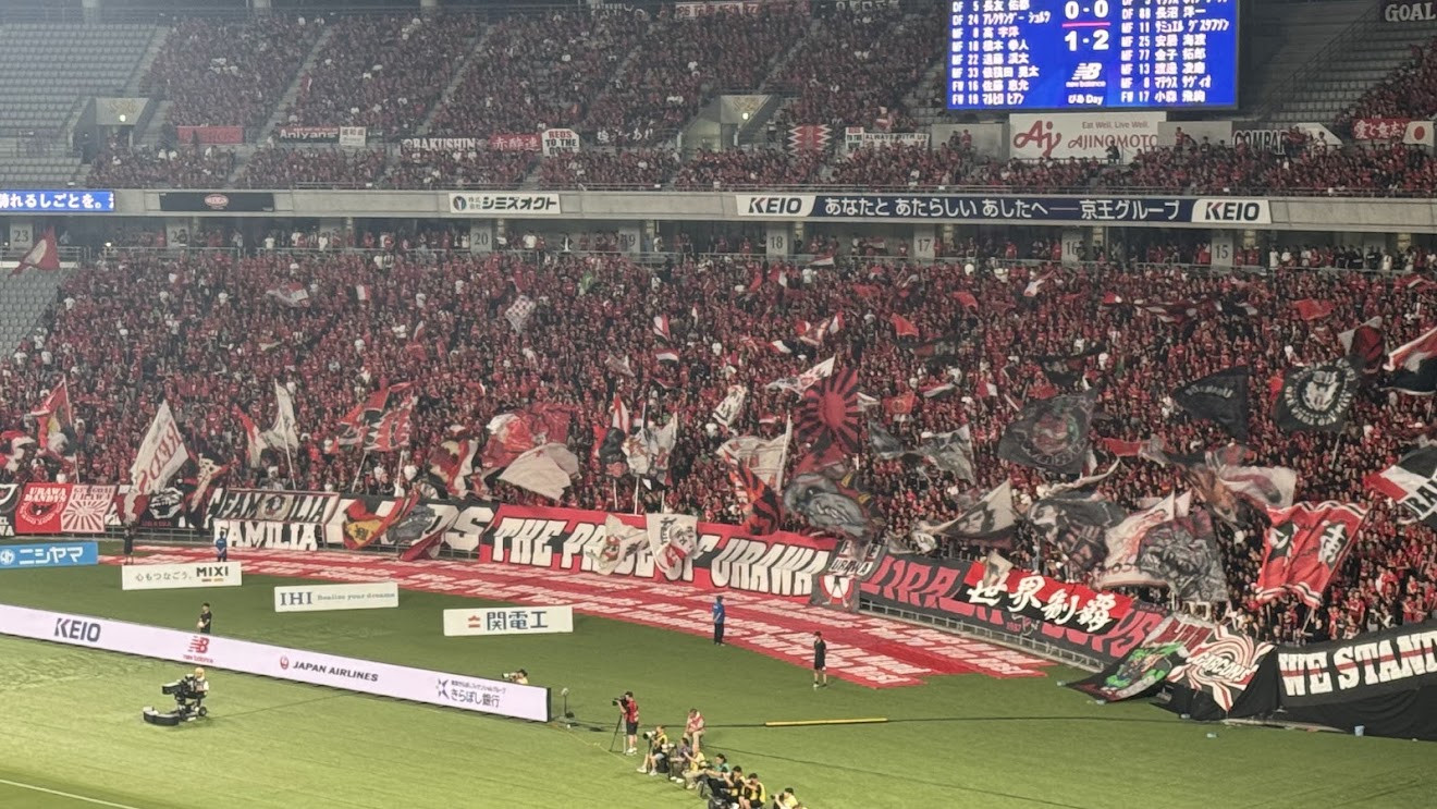 Urawa Reds supporters filling the stands with flags and a THE PRIDE OF URAWA banner at a J.League match
