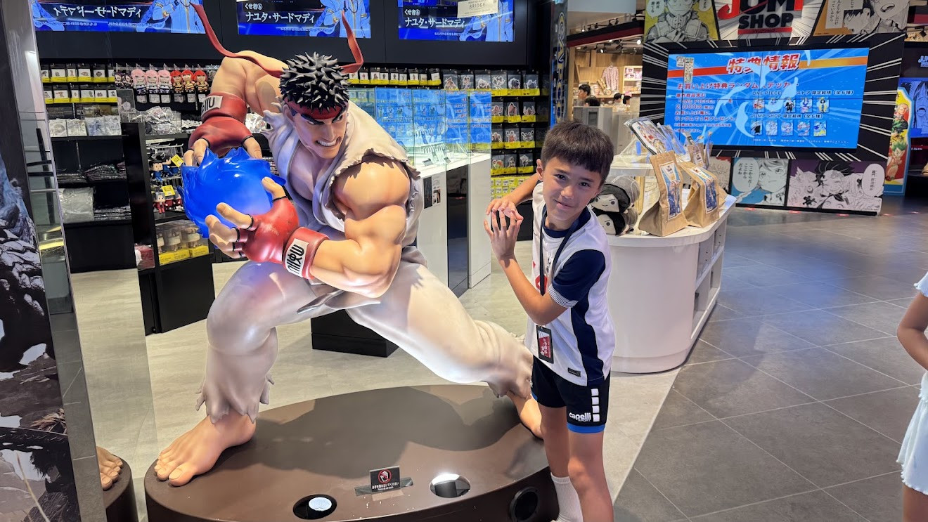 My son posing next to a statue of Ryu from Street Fighter throwing a hadoken at a Jump Shop