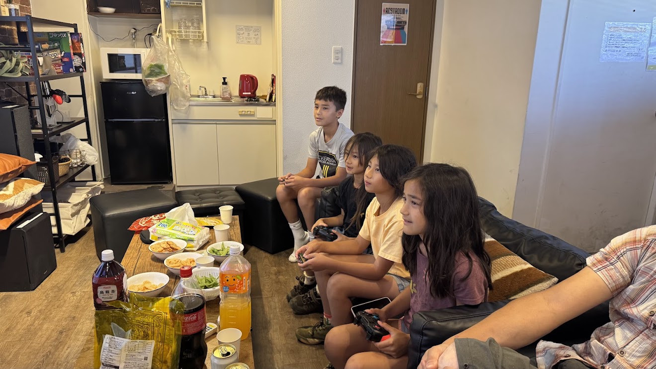 Kids sitting on the floor playing video games together at a friend’s place, with snacks on the table