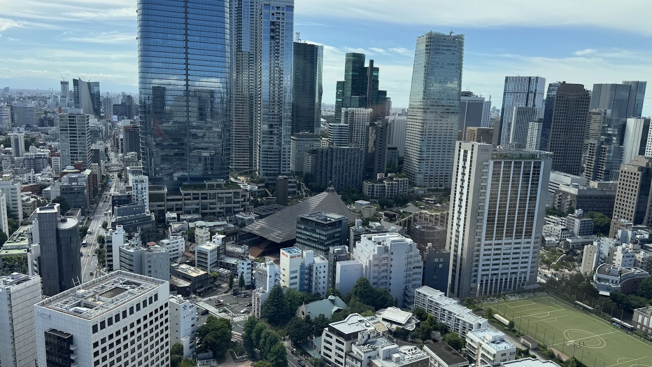 A view from high up over Tokyo toward a cluster of glass skyscrapers and city blocks