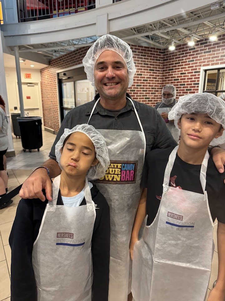 Adam and the kids in aprons and hairnets at Hershey's Create Your Own Candy Bar